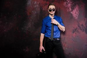 studio porträtt av snygg professionell fotograf man med kamera, bära på blå skjorta och slips, solglasögon. foto
