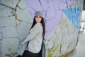 snygg brunett flicka i grå mössa, casual street style på vinterdag mot färgad vägg. foto