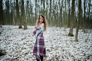 lockigt söt blond flicka med krans i rutig pläd vid snöig skog i vinterdag. foto