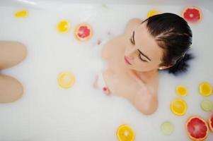 sexig brunett tjej på badrummet med mjölk och frukt. ungdomsbad för kroppen. foto