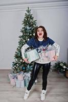 flicka bär varm tröja bakgrund nyår träd med presenter lådor till hands på studio. glad vintersemester koncept. foto