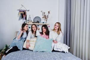 fyra söta vänner flickor bär på varma tröjor och svarta byxor på sängen på nyår inredda rum på studio, leka med kuddar. foto