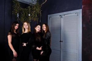 fyra söta vänner flickor bär svarta klänningar mot juldekoration. foto