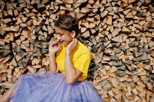ung rolig tjej med ljus smink, som sagoprinsessa, bär på gul skjorta och violett kjol mot träbakgrund. foto