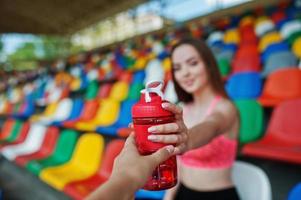 fitness sportig tjej i sportkläder sitter på stadion stolar utomhussporter. glad sexig kvinna med sport flaska mockup.close upp hand med bootle. foto