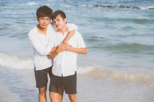 homosexuella porträtt ungt asiatiskt par står kram tillsammans på stranden på sommaren, asien gay turism för fritid och koppla av med romantisk och lycka i semestern till sjöss, hbt-koncept. foto