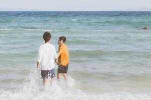 homosexuella porträtt ungt asiatiskt par springer med glada tillsammans på stranden på sommaren, asien gay turism för fritid och koppla av med lycka i semestern till sjöss, hbt juridiskt koncept. foto