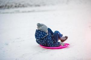 söt liten flicka med tefat slädar utomhus på vinterdagen. foto