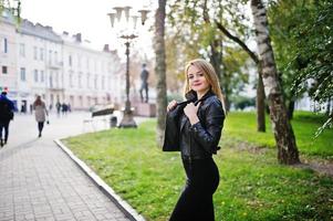 elegant blond flicka bär på svart skinnjacka poserar på gatorna i staden. foto