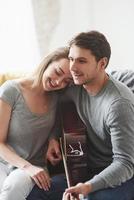 tjejen är nöjd. spelar på akustisk gitarr för flickvännen i vardagsrummet i nya huset foto