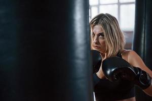 ilska och energi. kvinnlig boxare slår i väskan. blondin tränar på gymmet foto