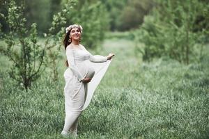 i parken. vacker gravid kvinna i klänning har en promenad utomhus. positiv brunett foto