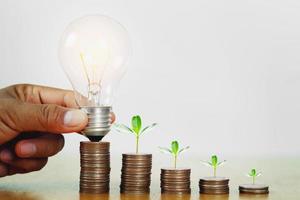 hand som håller glödlampa med växt växande steg på pengar. koncept ekonomi redovisning och spara energi foto