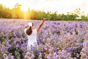 ung kvinna avkopplande och njuter i blommande blommor fältet på morgonen foto