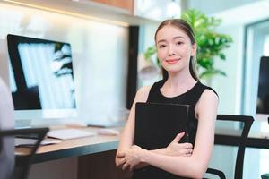 porträtt av framgångsrik och leende ung affärskvinna som håller fil och känner sig självsäker och stolt när hon står på kontoret och tittar på kameran foto