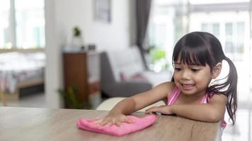 glad liten asiatisk tjej som lär sig städa med en trasa i vardagsrummet hemma. hushållsarbete och hushållskoncept. foto
