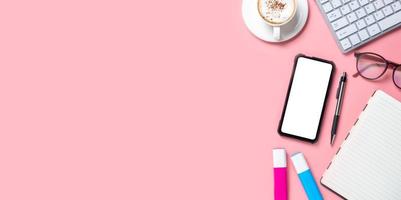 skrivbord med tangentbordsdator, smart telefon med tom skärm, kopp kaffe, glasögon, penna, anteckningsbok på rosa bakgrund, ovanifrån med kopieringsutrymme, mock up. foto