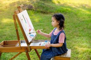 en liten flicka sitter på träbänken och målad på duken placerad på ett ritställ foto