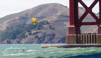 gul segel och kitesurfer under den orange strukturen av Golden Gate-bron på San Francisco-bukten foto