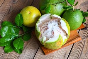 färsk grön pomelo skalad och blad från pomeloträd, pomelofrukt på träplattabakgrund, pummelo, grapefrukt på sommaren tropisk frukt i thailand foto