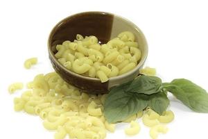 rå makaroner är en utsökt ingrediens i det italienska köket som är populär över hela världen och är en europeisk favorit och basilikablad i en tallrik på vit bakgrund. foto