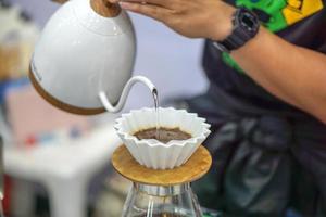 närbild händer av barista göra och hälla färskt dopp kaffe från vattenkokaren för kunden i ett kafé. foto