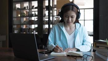 leende asiatisk ung kvinna som använder headset tittar på laptop skärm lyssna och lära sig onlinekurser. glad kinesisk affärskvinna med hörlurar videosamtal för kundtjänst foto