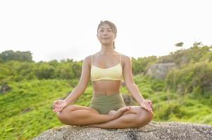 vacker asiatisk kvinna i sportkläder gör yoga på bergstoppen vid havet efter vandring, resor och meditationskoncept. foto