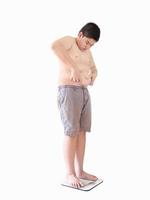 mjukt fokus av fet pojke svika sin fetma när han står på vågmaskinen isolerad över vit bakgrund och inkluderad urklippsbana. foto