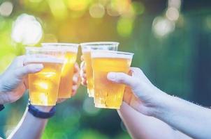 firande öl hurrarop koncept - närbild händer som håller upp glas öl av folkgrupp i utomhusfest under deras segertävling eller framgångsrika uppgiftsmöte foto