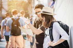 asiatisk ryggsäck par turist håller stadskarta som korsar vägen - resor människor semester livsstilskoncept foto