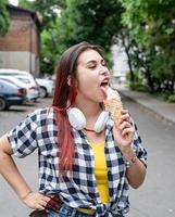 gladlynt trendig kvinna med rött hår som äter glass på gatan i sommarvärmen foto