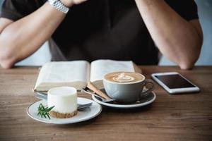 slappna av asiatisk man dricker kaffe och läser bok i ett kafé i modern stil - människor med kaffekopp enkelt livsstilskoncept foto