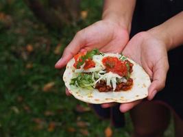 närbild av taco mexikansk mat på händerna ung kvinna som står i trädgården foto