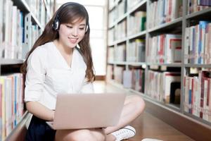 asiatisk vacker kvinnlig student som studerar i bibliotek med laptop foto