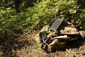 smarttelefonen laddas med en bärbar laddare powerbank på en solpanel, på bakgrunden av en ryggsäck när du reser foto