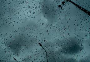 regndroppar på genomskinligt glas mot oskärpa mörk stormig himmel och elstolpe. regndroppar på vindrutan. vindruta fönster av bil med regndroppar. storm dag. ledsen och deprimerad abstrakt bakgrund. foto