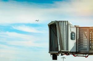 jet bridge efter kommersiella flygbolag lyfter på flygplatsen och planet flyger i den blå himlen och vita moln. ombordstigningsbro för flygplanspassagerare dockad. det internationella flygbolagets avgångsflyg. foto