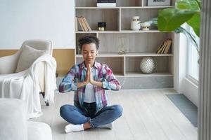 ung tonåring afroamerikansk flicka utövar yoga i lotusställning hemma. hälsosam livsstil, meditation foto