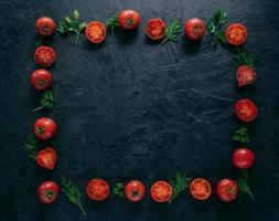 sammansättning av röda tomater och grön färsk persilja och dill liggande på mörk bakgrund i form av ram. vegetarisk mat koncept. ledigt utrymme i mitten foto
