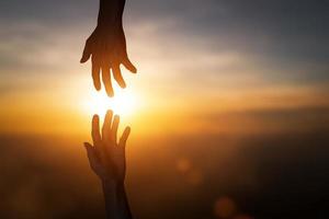 siluett av att nå, ge en hjälpande hand, hoppas och stödja varandra över suddiga solnedgångshimmelbakgrund. foto