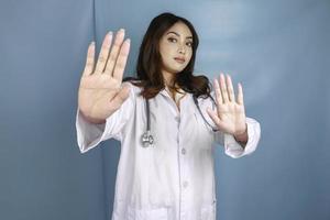 allvarlig asiatisk kvinnlig läkare med stetoskop och vit rock, visar stopptecken. foto