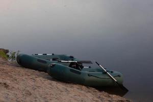 två gummibåtar med fiskeredskap tidigt på morgonen under dimman, parkerade vid flodens strand. foto