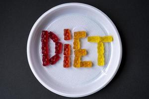 vit plasttallrik med text diet från söt gelé. söt frukt gummibjörnar. hälsosam kost, skräpmat, diet och bantning koncept, ovanifrån. foto