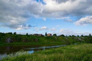 en by vid flodstranden med ljusgrönt gräs och en vacker himmel. foto