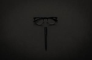 glasögon och penna i modern livsstil på mörk bakgrund för minimalistisk platt låg svart koncept. foto