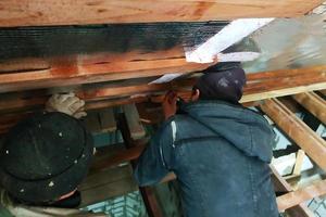 mästarteamet installerar husets tak och skruvar i synnerhet skruvarna i brädorna för att fixera foliefilmen och mineralullen foto