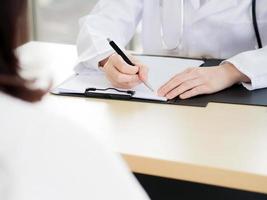 en närbild av handen på en kvinnlig läkare eller sjuksköterska använder en penna som skriver information eller något med en suddig kvinnlig patient i förgrunden. foto