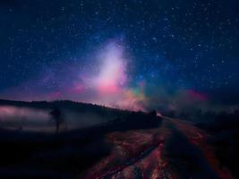 Vintergatan och rosa ljus vid bergen. natt färgglada landskap. stjärnhimmel med kullar. vackert universum. rymdbakgrund med galax. resor bakgrund foto