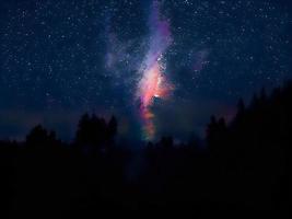 Vintergatan och rosa ljus vid bergen. natt färgglada landskap. stjärnhimmel med kullar. vackert universum. rymdbakgrund med galax. resor bakgrund foto